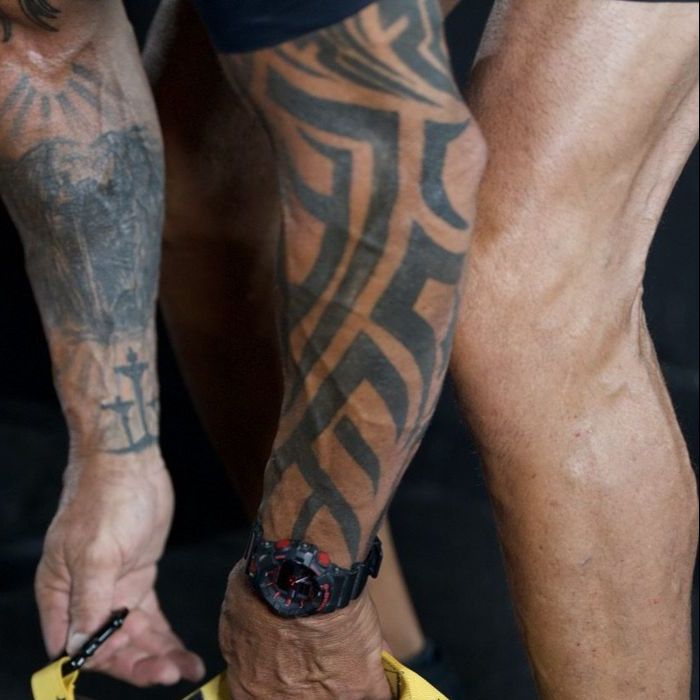 Coach gripping kettlebell handles, tattooed forearm and calf